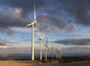 a row of six wind turbines in a field, clouds in the background