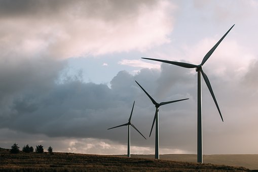 3 wind power turbines in a field, cumulus clouds in the background at sunset