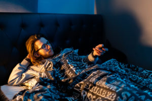 Propping head on arm, young man watches TV in bed before trying to sleep.