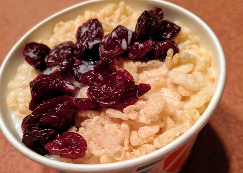 A paper cereal bowl filled with crisp rice cereal, dried cherries, and milk