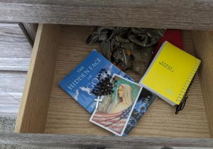 Open drawer with sacred and personal objects like a rosary, a prayer card, dream journal, and spiritual book. 