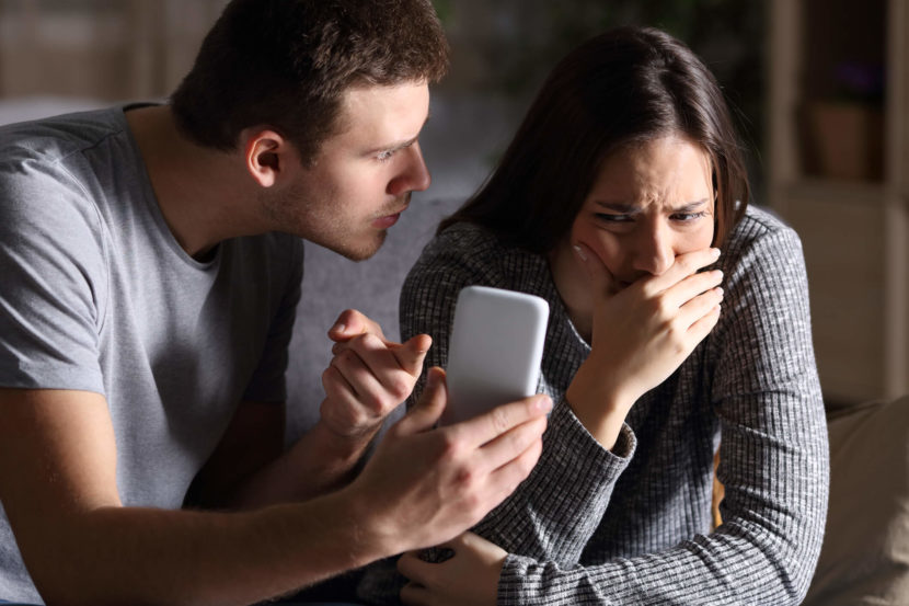 a man hold a phone up accusingly while a woman cries.